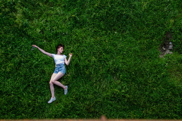 Portrait of happy cute young woman with short hair in casual black and white striped shirt, red round eyeglasses lying down on green grass and looking at camera through glasses.outdoor summertime shot