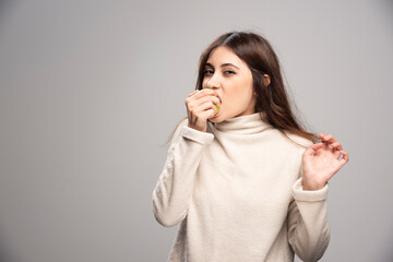 A young girl biting a green apple on a gray background