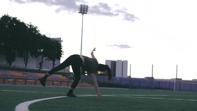 Close up beautiful Caucasian female in sporty clothes practicing wheel gymnastic exercise at the stadium. Yoga concept. Female gymnast at stadium practicing, doing fitness