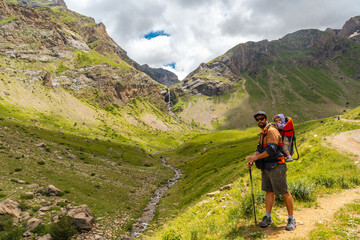 Fototapeta na wymiar A young man with his son in his backpack, Salto de Tendenera Waterfall in the Ripera Valley, Pyrenees