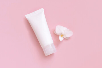 White cream tube near white orchid flower on light yellow top view. Mockup. Skincare product