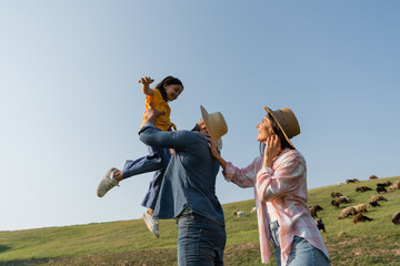 woman smiling near farmer playing with child in green pasture under blue sky. © LIGHTFIELD STUDIOS