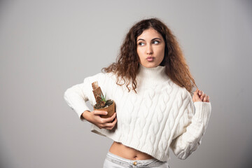 Young woman gardener holding a plant on a gray wall