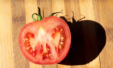 A red tomato, cut. Half a tomato on a bamboo chopping board. Healthy, ripe vegetables.