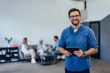 Elegantly dressed man, holding a tablet, smiling for the camera while being at the co-working space.