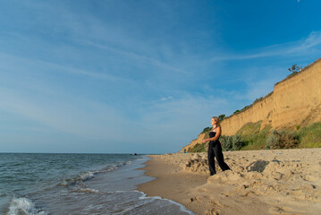 Beautiful fashionable female in black suit is walking on sandy beach. See view