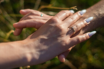 Close up of the bride and groom hold hands on the field showing off their rings.