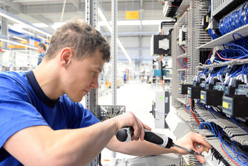 young apprentice assembles components and cables in a factory in a switch cabinet - workplace...
