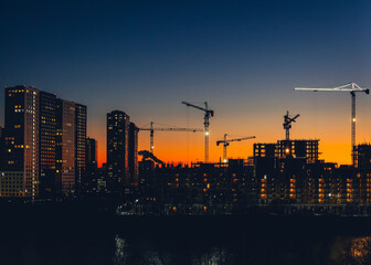 Naklejka premium Metropolitan skyline with tower cranes building high-rise residential buildings in evening time. Steel frame structure in sunlight. Industrial background. Lifestyle