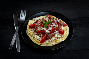 Italian spaghetti pasta with tomato sauce, parmesan cheese and basil served on rustic kitchen table