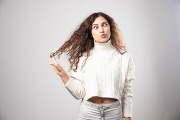 Young woman in white sweater doing funny face over a white wall