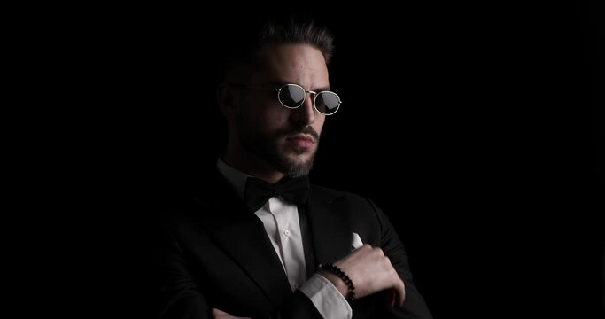 handsome young groom with sunglasses folding arms, holding hand to chin and thinking, looking over shoulder and smiling in the dark
