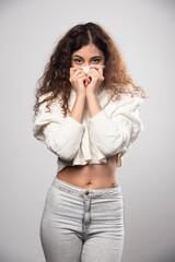 Young woman in white sweater standing over a white wall