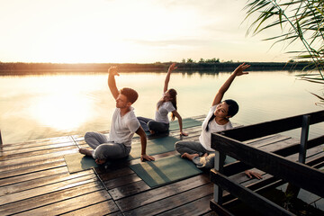 Group of people doing yoga exercises by the lake at sunset.	