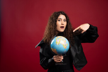 Cheerful woman pointing at globe over red background