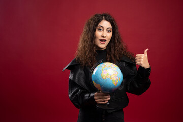 Cheerful woman holding globe and giving thumbs up