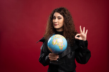 Cheerful woman holding globe and giving ok sign