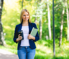 Young smiling beautiful woman in park with tablet gadget and wireless headphones enjoying - green energy concept, remote work