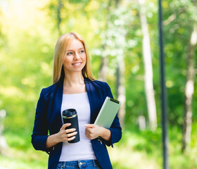 Fototapeta premium Young smiling beautiful woman in park with tablet gadget and wireless headphones enjoying - green energy concept, remote work
