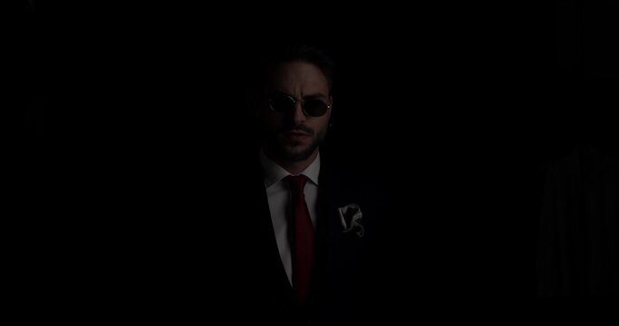 handsome cool man with in suit with handkerchief looking to side, pulling glasses and looking over, adjusting tie and walking away in the dark