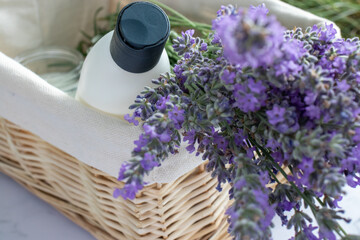 Shampoo bottle, aromatic candle and bunch of lavender flowers in wicker basket on white table background. Birthday, wedding, bridal shower gift box with hygienic cosmetic products. Top view. 