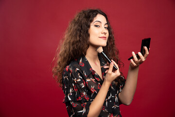 Elegant woman applying bronzer with brush on red background