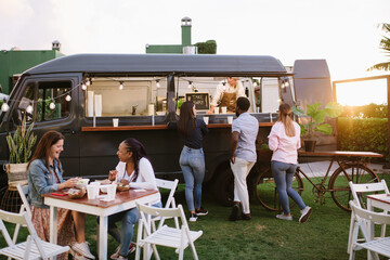 People gathering near food truck at sunset