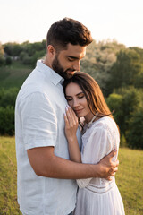 happy woman with closed eyes leaning on chest of bearded man outdoors.