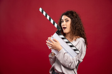 Brunette woman holding clapperboard on red background