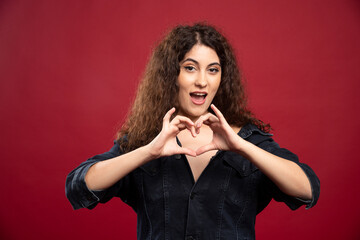Fototapeta premium Beautiful curly woman giving heart gesture on red background
