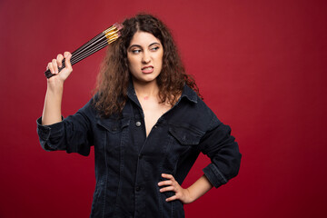 Angry artist holding paintbrushes on red background