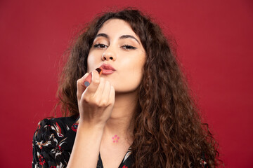 Curly woman applying lipstick on red background