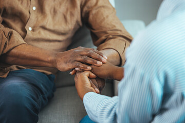 Close up black woman and man sitting on couch two people holding hands. Symbol sign sincere...
