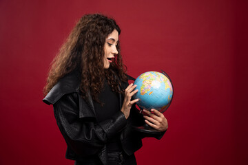 Young woman looking at globe on red background