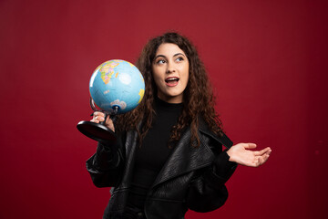 Naklejka premium Cheerful woman holding globe on red background