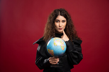 Cheerful woman holding globe on red background