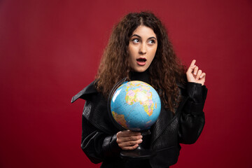 Cheerful woman holding globe on red background