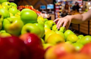 Woman's hand choosing apple on fruits shelf in supermarket