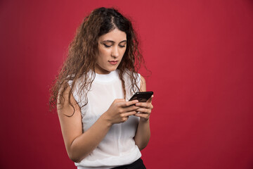 Surprised woman is typing something on her mobile phone on red background