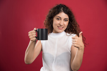 Woman holding hot dark cup and shows thumb up on red background