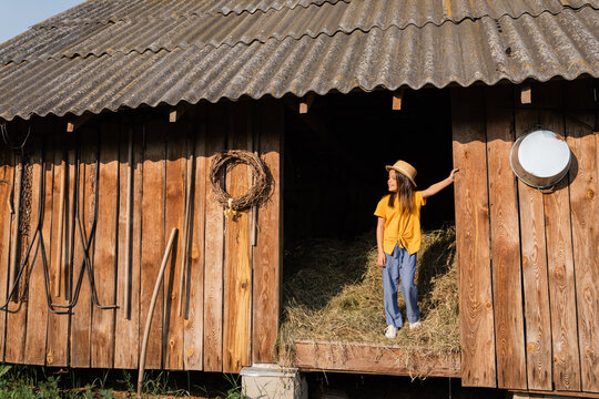 full length of girl standing on hey in wooden barn and looking away.