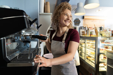 Young caucasian female barista making coffee in the cafe and looking away with a smile