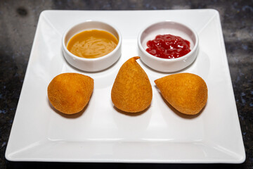 Traditional Coxinha of Chicken is a traditional Brazilian snack. In selective focus, with ketchup and yellow mustard on the plate. 