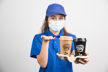 Fototapeta na wymiar Woman in blue uniform with medical mask holding two cups of coffee on white background
