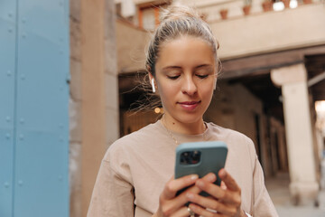 Image of pretty blonde woman looking and have chat on phone . Caucasian cute lady wearing brown t-shirt staying in headphones 