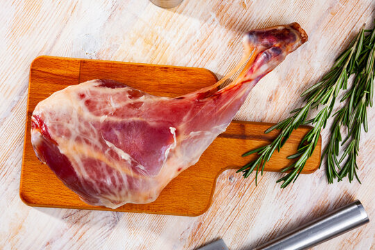 Fresh raw leg of milk-fed lamb with condiments ready for cooking on wooden table