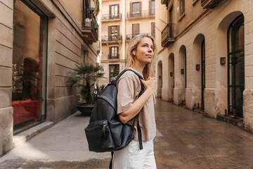 Image of attractive european woman walking in the city .Caucasian young blonde girl holding black backpack and look away