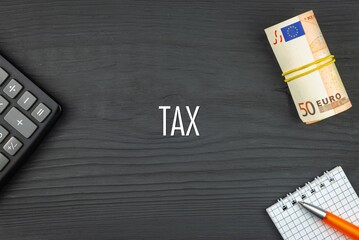 TAX - word (text) and euro money on a wooden background, calculator, pen and notepad. Business concept (copy space).