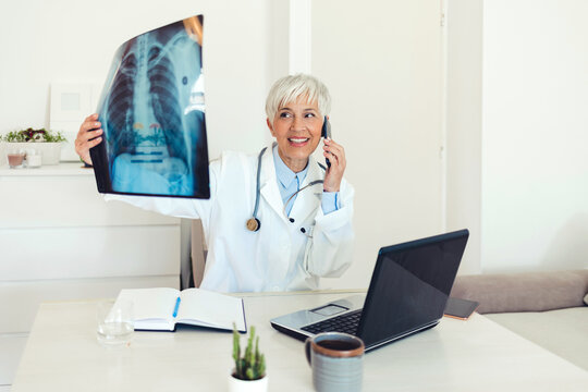 Female radiologist holds x-ray while calling patient. Female doctor uses phone to talk with patient about x-ray results.