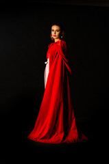 Naklejka premium beautiful woman red cloak with red flowers roses in studio. Woman Red Riding Hood. Dramatic and fantastic shooting,fashionable toning. Like a princess